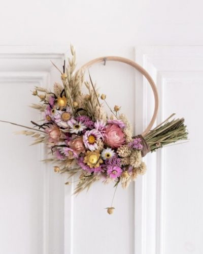 Handmade dried flower wreath with pink, and yellow flowers, and a wooden hoop, styled as a rustic floral wall or door decoration.
