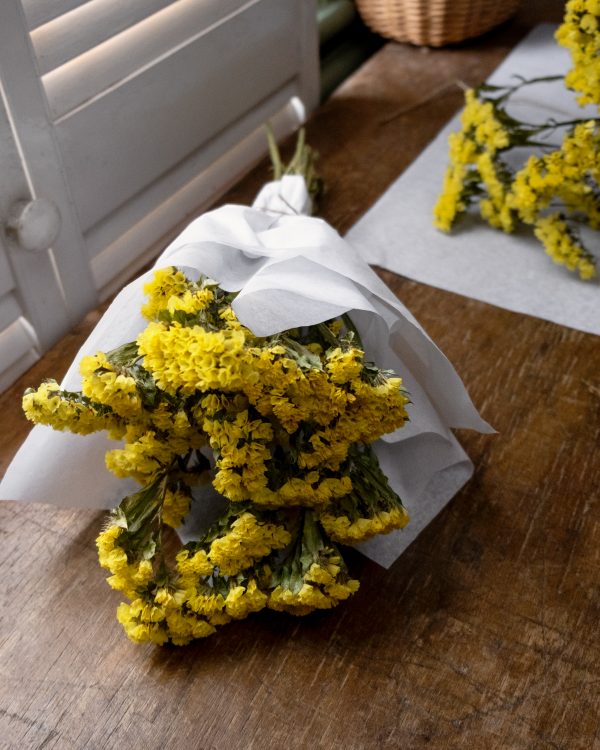 bunch of yellow statice dried flowers wrapped in white tissue paper tied with twine laid on wooden table top