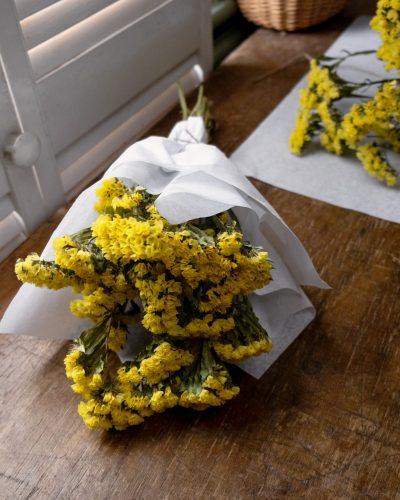 bunch of yellow statice dried flowers wrapped in white tissue paper tied with twine laid on wooden table top