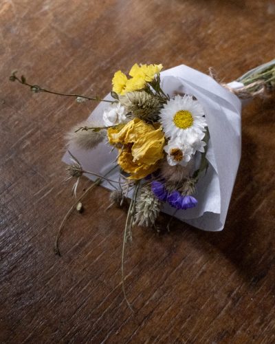 mini blue and yellow dried flower posy laid on a wooden table wrapped in white tissue and tied together with twine