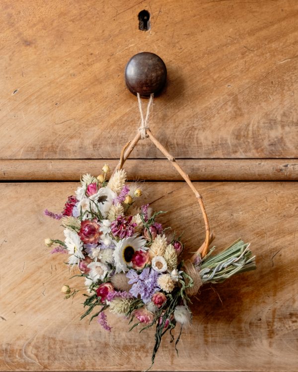 Mini tear drop shaped willow wreath. The wreath is half covered in dried flowers and hung on a wooden drawer knob