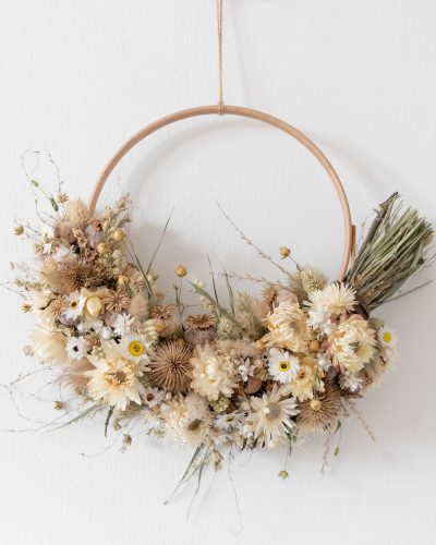 white strawflower and teasel dried flower half wreath. The wreath is made from a wooden hoop and the wreath is hung on the back of a white door