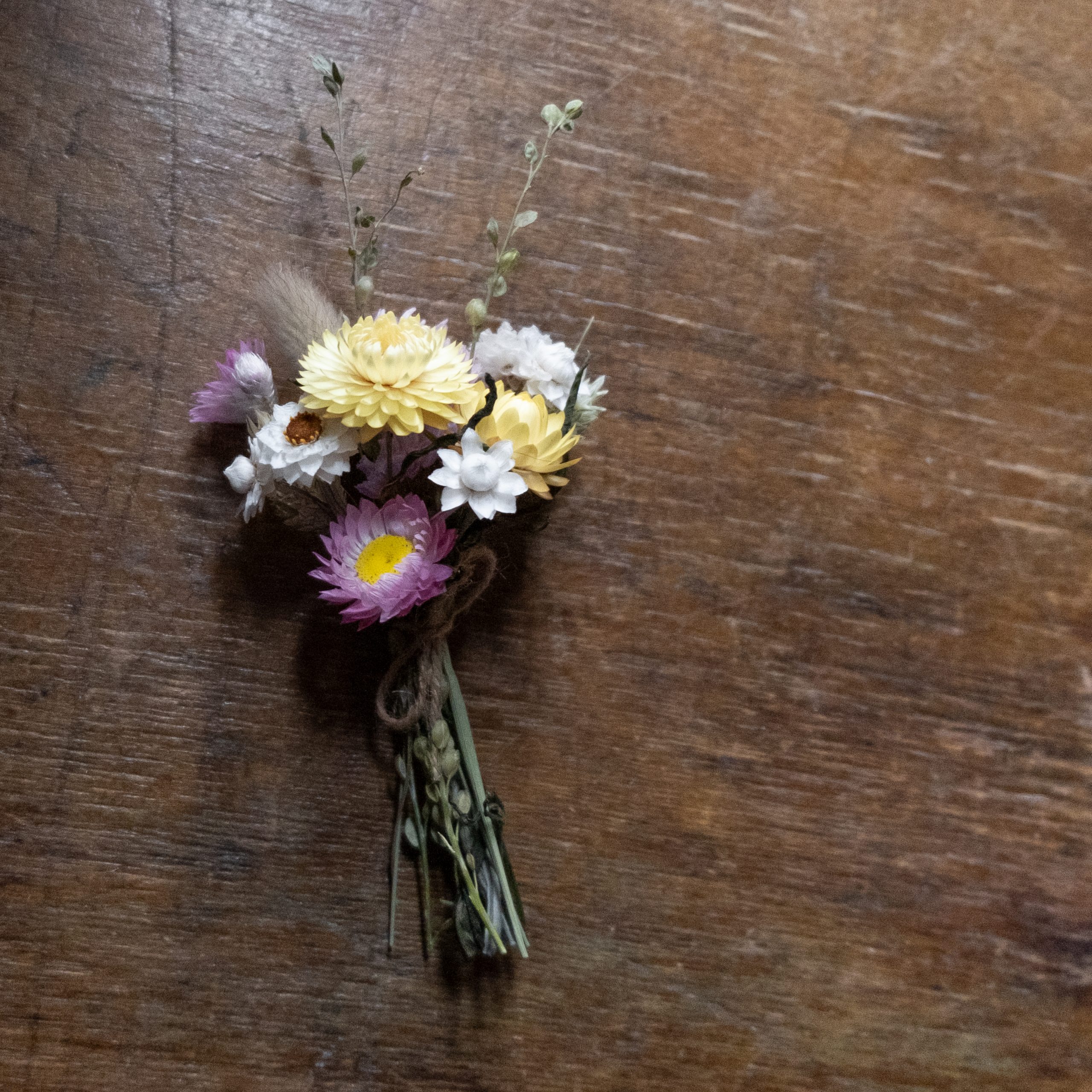 mini bouquet posy of pink yellow and white dried flowers tied with twine laid on a natural wood surface