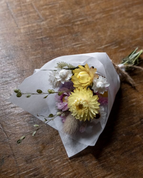 pink and yellow small mini posy in on a wooden surface wrapped in white tissue paper tied with twine