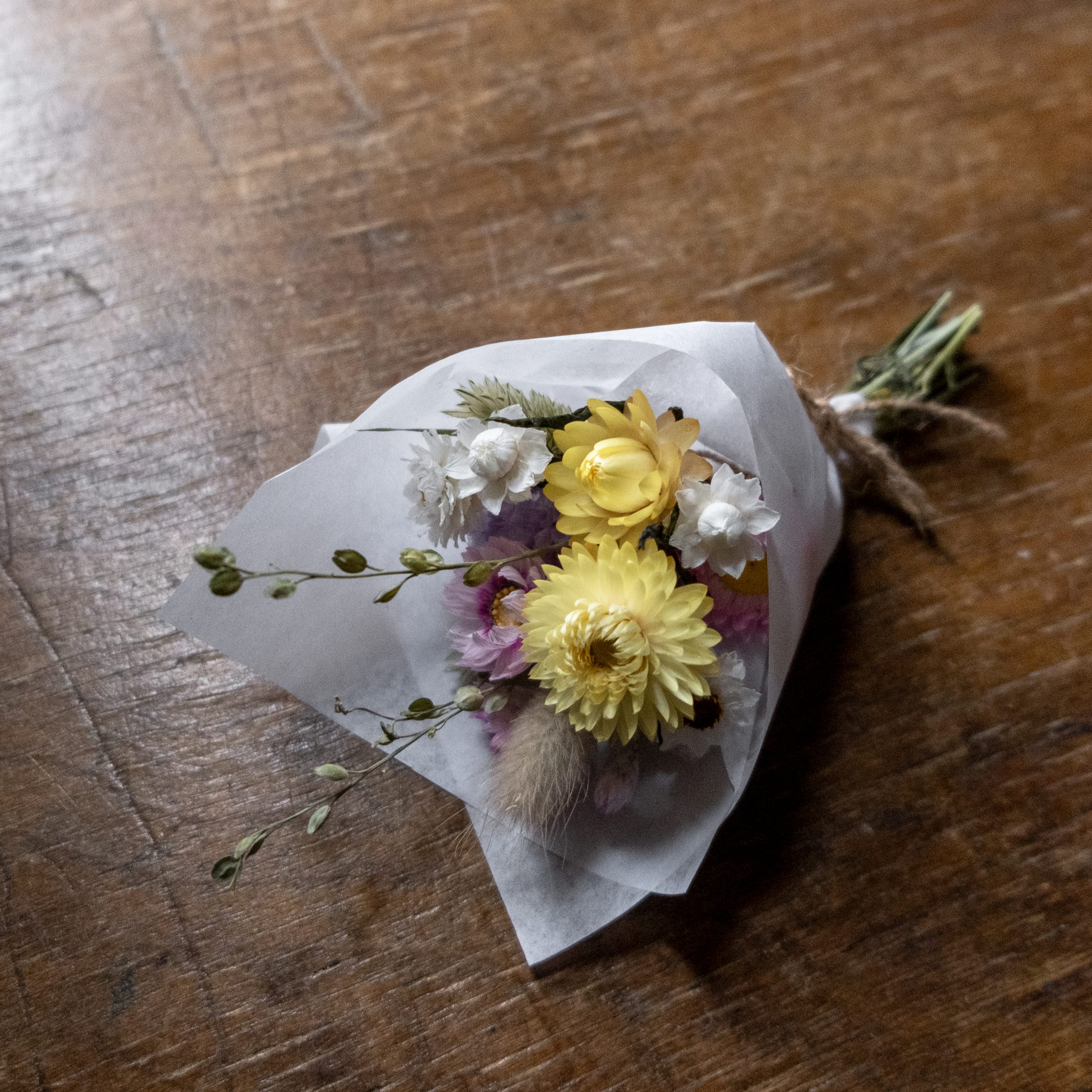 pink and yellow small mini posy in on a wooden surface wrapped in white tissue paper tied with twine